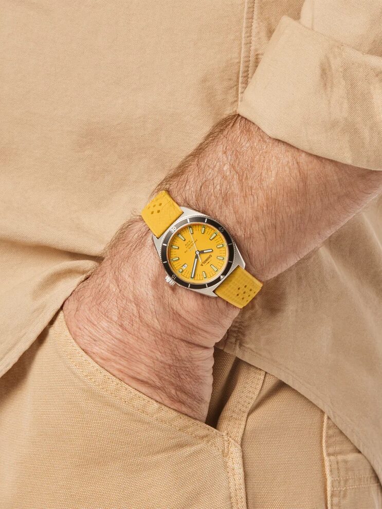 A person wearing a yellow watch with a yellow strap, beige shirt, and beige pants, with their hand in their pocket.