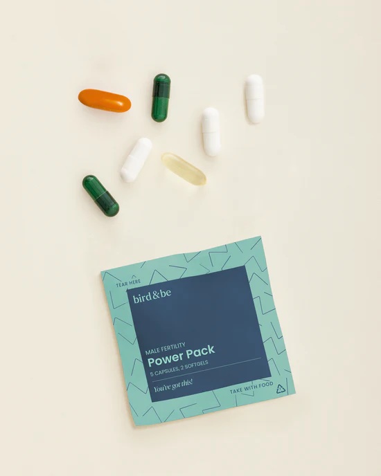 A packet labeled "Male Fertility Power Pack" by bird&be is displayed with seven assorted capsules and softgels arranged above it on a light background.
