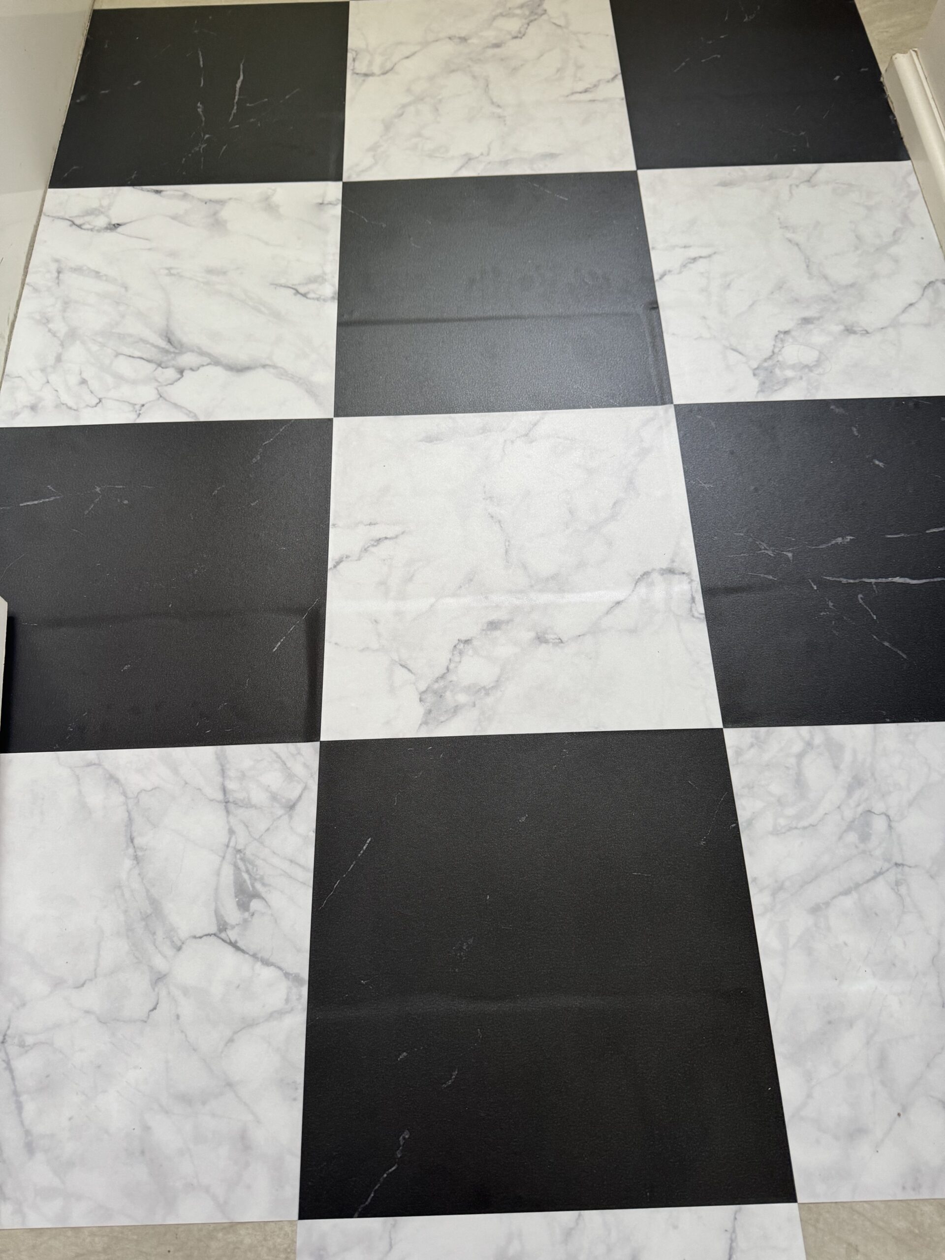 A black and white checkered floor with a marble pattern on the white tiles and a matte finish on the black tiles.