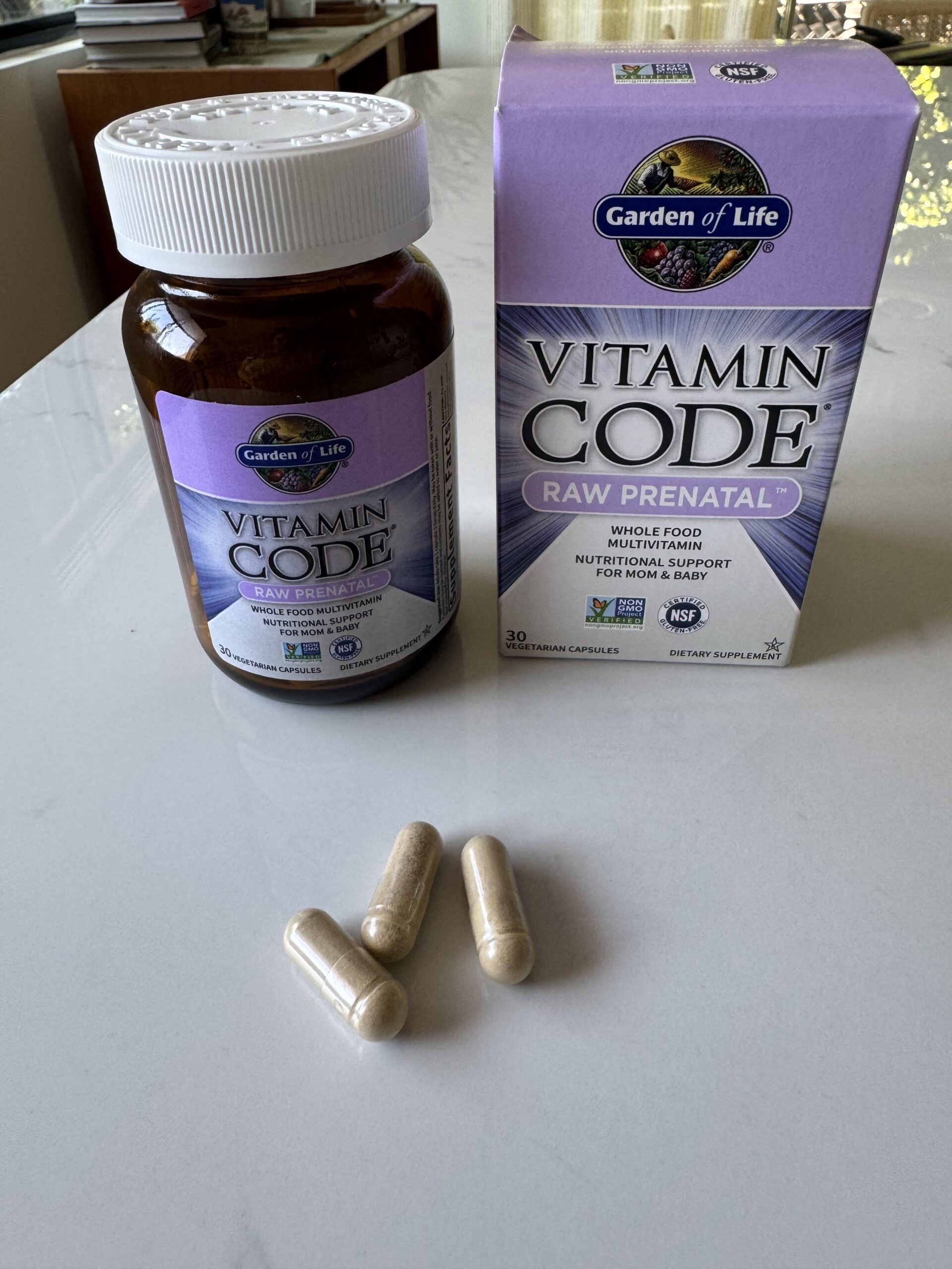 A bottle and box of Garden of Life Vitamin Code Raw Prenatal capsules, a trusted prenatal vitamin, sit on a table with three capsules placed in front.