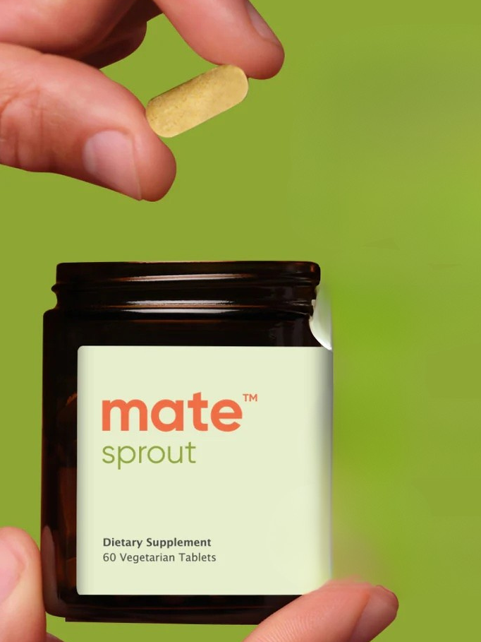 A hand holds a yellow tablet above an open dark jar labeled "mate sprout, Dietary Supplement, 60 Vegetarian Tablets" against a green background.