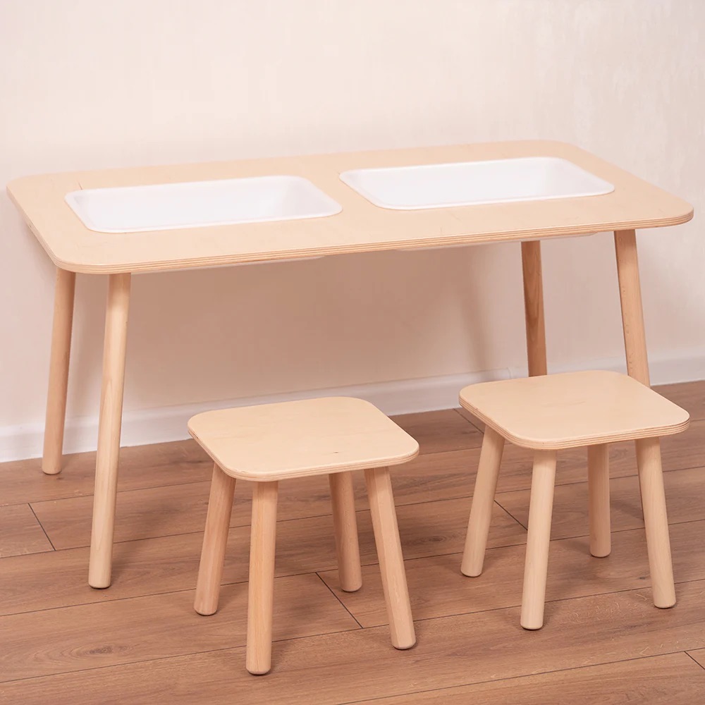 A wooden table with two built-in white plastic trays and two matching wooden stools, placed on a wood floor against a light-colored wall.
