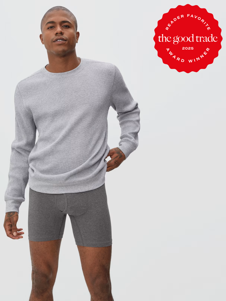 A man wears a light gray long-sleeve shirt and dark gray boxer briefs, standing against a plain background next to a red "The Good Trade 2025 Award Winner" badge.