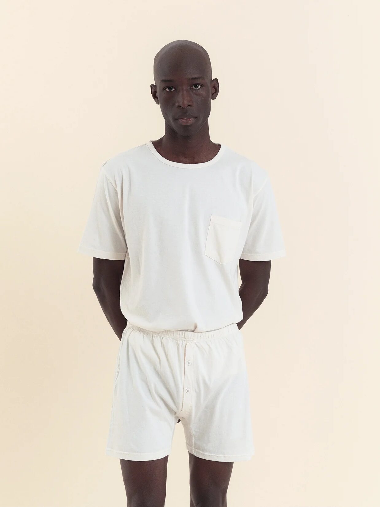 A person stands facing forward, wearing a plain white T-shirt and matching white shorts against a neutral background.