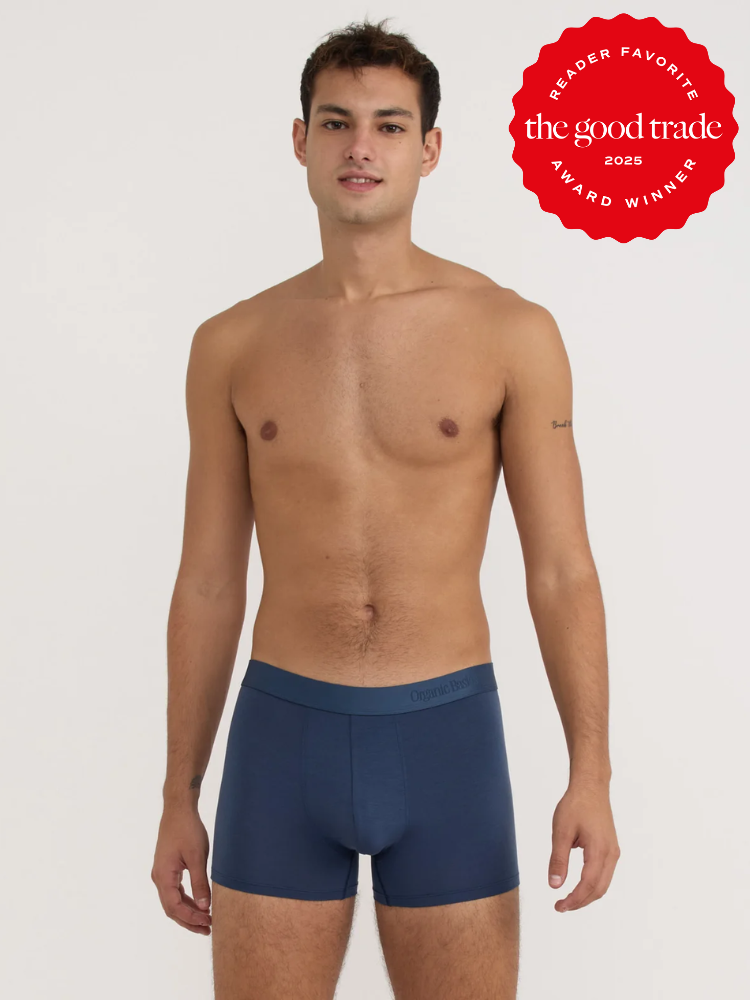 A man stands against a plain background wearing navy blue boxer briefs. A red badge in the top right corner reads "the good trade reader favorite award winner 2025.
