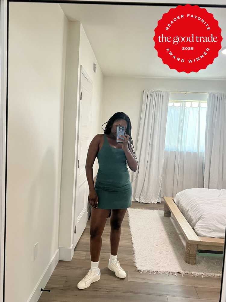 A person stands in front of a mirror taking a selfie, wearing a green dress and white shoes in a bedroom. A "The Good Trade 2025 Award Winner" badge is visible in the top right corner.