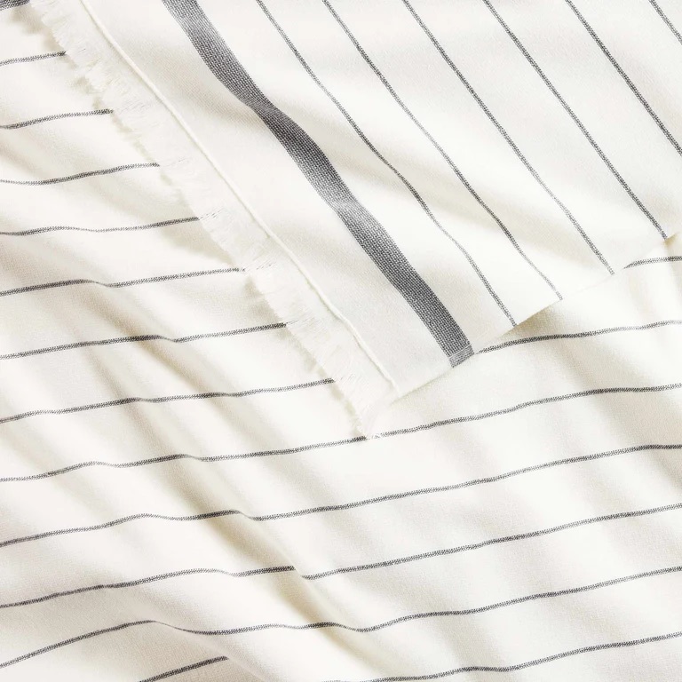 Close-up of a white fabric with thin black horizontal stripes and a visible selvage edge.