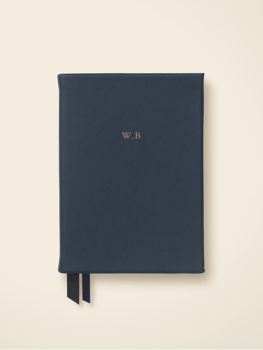 A closed, dark blue notebook with "W.B" embossed in gold on the cover and two black ribbon bookmarks, photographed against a plain light background.
