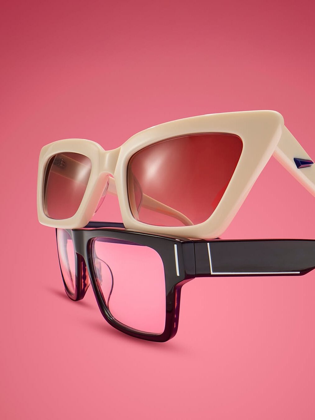 Two pairs of sunglasses with pink lenses, one beige and one black, are stacked against a solid pink background.