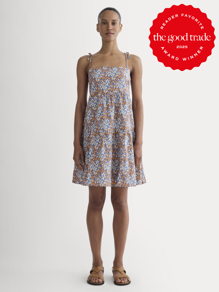 A woman stands facing forward in a sleeveless, floral-print dress with tie straps and sandals. A red "The Good Trade 2025 Award Winner" badge is in the top right corner.