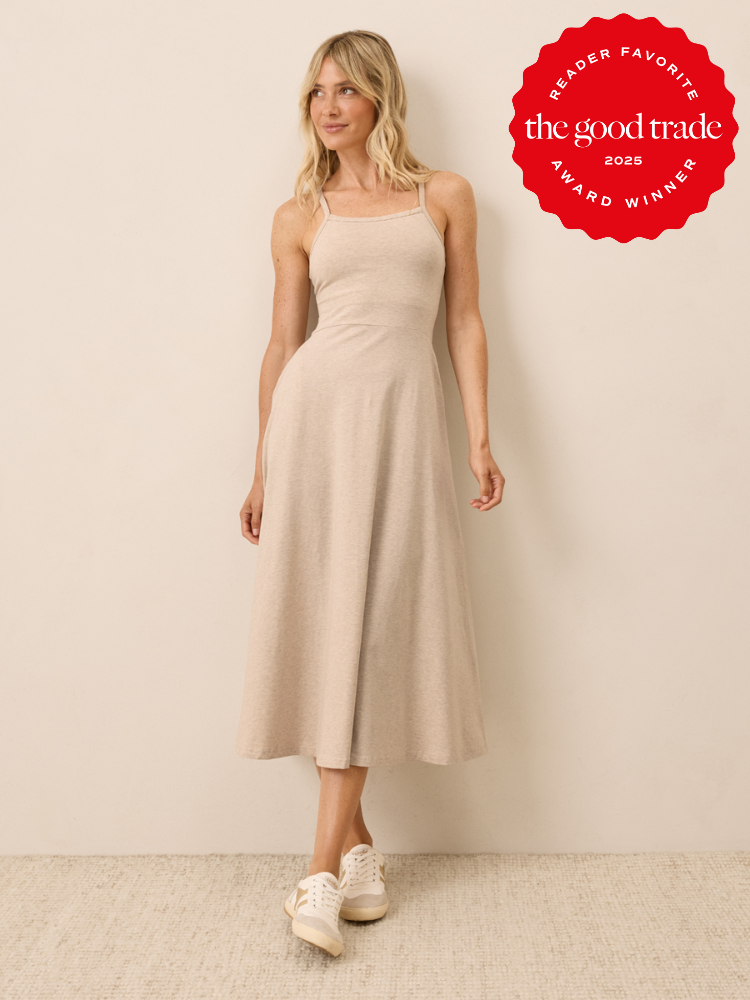 Woman wearing a sleeveless, light beige midi dress and white sneakers stands against a plain wall. A red "The Good Trade 2025 Award Winner" badge appears in the top right corner.