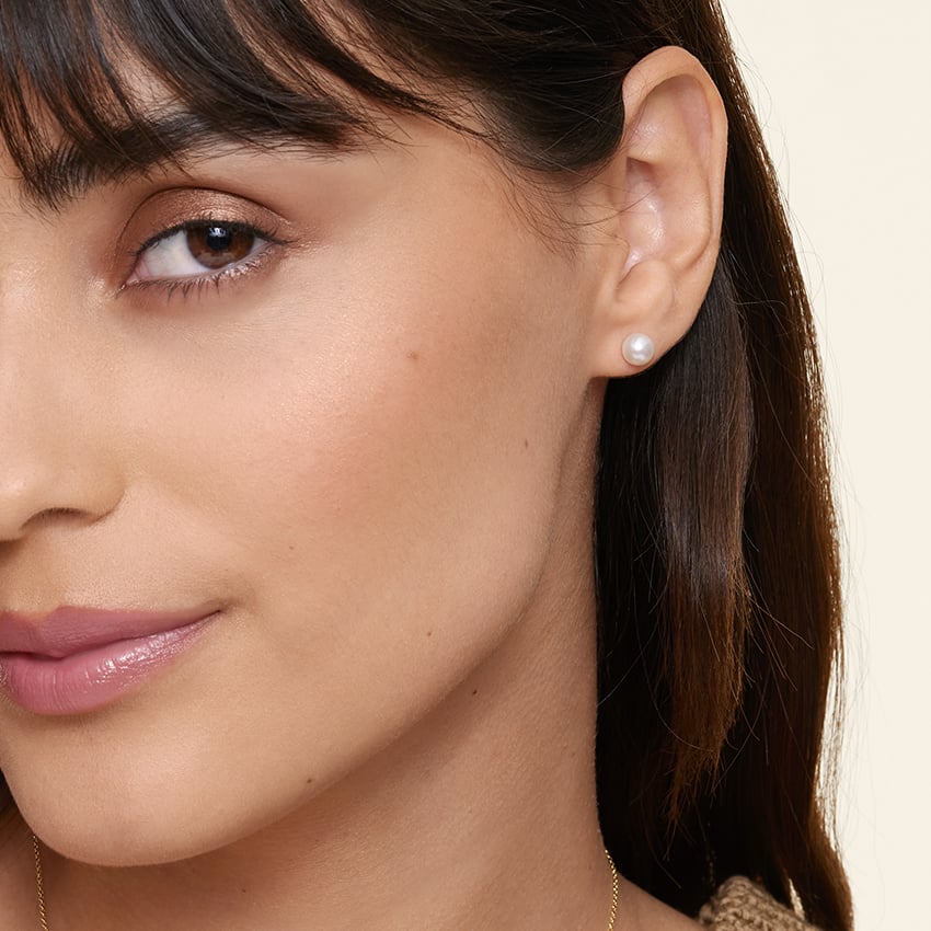 A woman with straight brown hair and natural makeup wears a small round pearl earring.