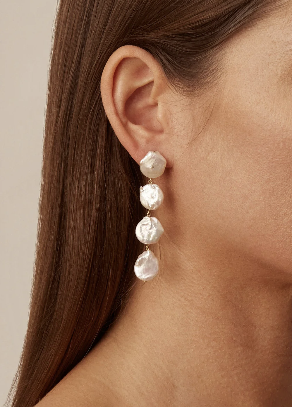 Close-up of a person wearing a long, dangling earring with four large, irregularly shaped white pearls.