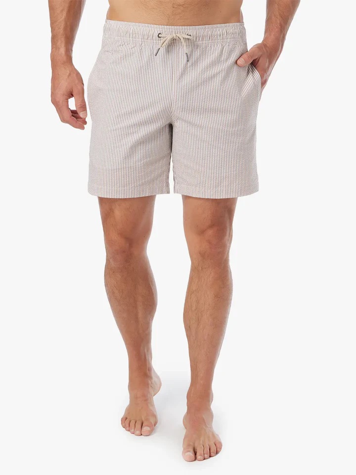 A man wearing light-colored, striped drawstring shorts stands barefoot against a plain white background.