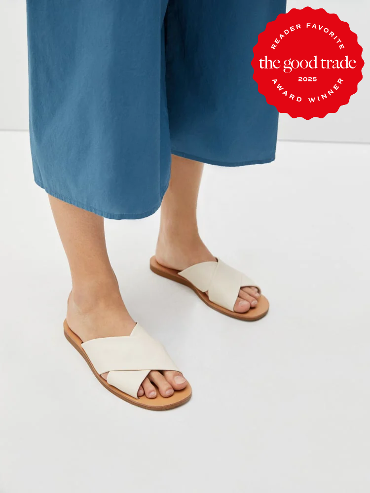 A person wearing cream-colored crisscross strap sandals and blue cropped pants stands on a light-colored floor. A red award badge appears in the top right corner.