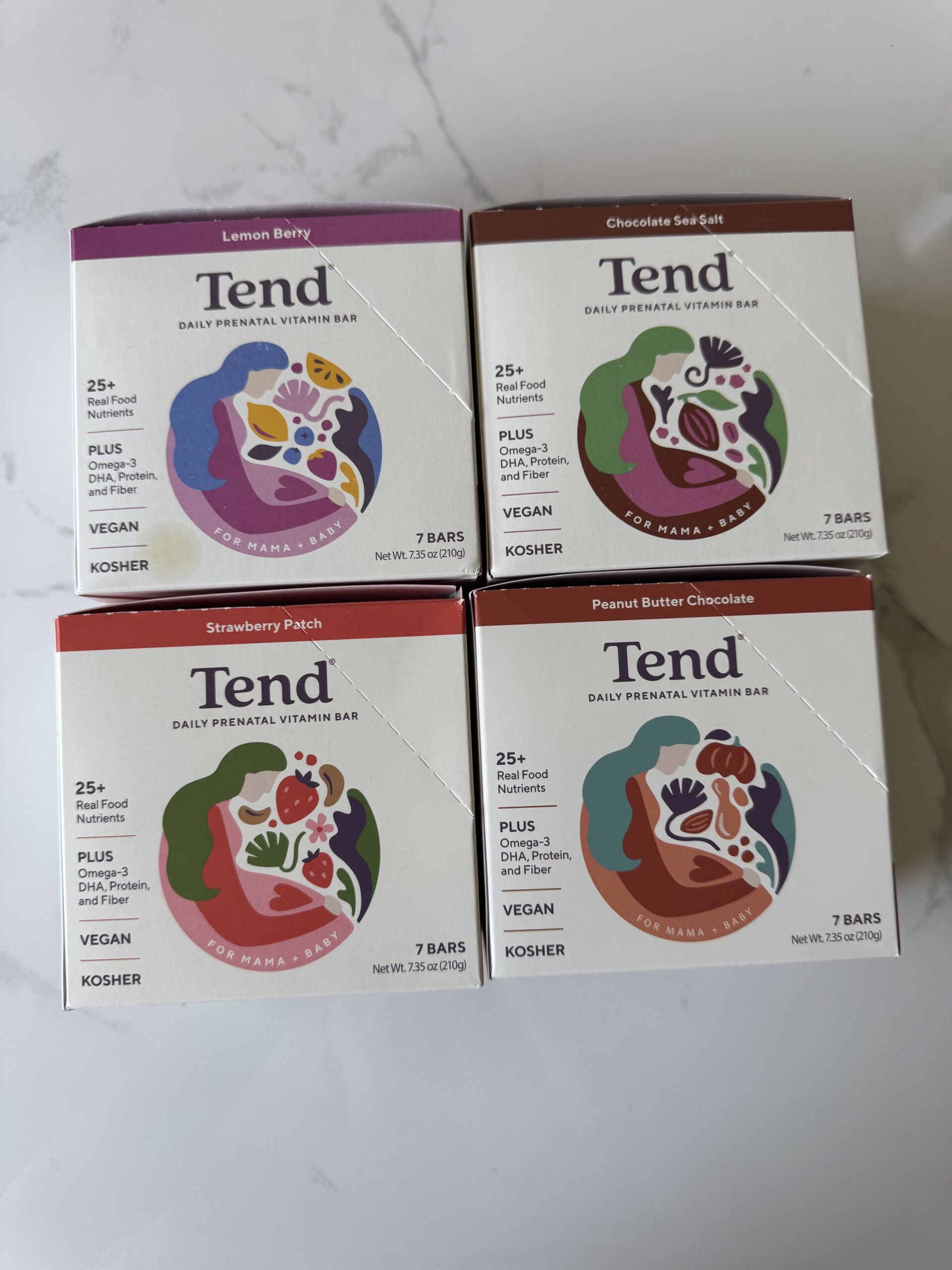 Four boxes of Tend Daily Prenatal Vitamin Bars, made with essential prenatal vitamin support, in Lemon Berry, Chocolate Sea Salt, Strawberry Patch, and Peanut Butter Chocolate flavors are arranged in a grid on a white surface.
