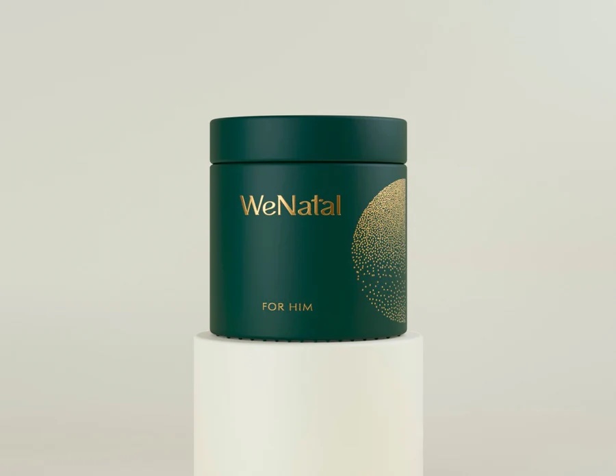 A dark green cylindrical container labeled "WeNatal FOR HIM" with gold lettering sits on a white pedestal against a light background.