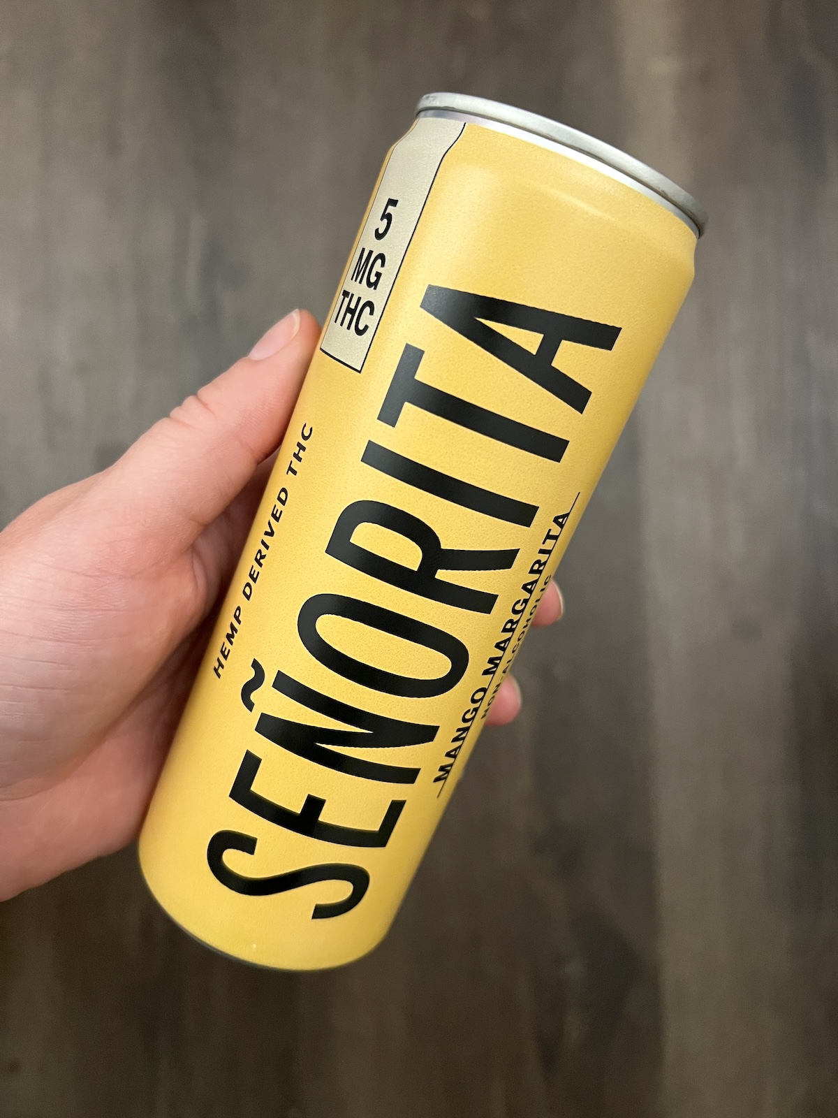 A hand holding a yellow can labeled "Señorita," marked with 5 mg THC and "Mango Margarita," against a blurred dark background.