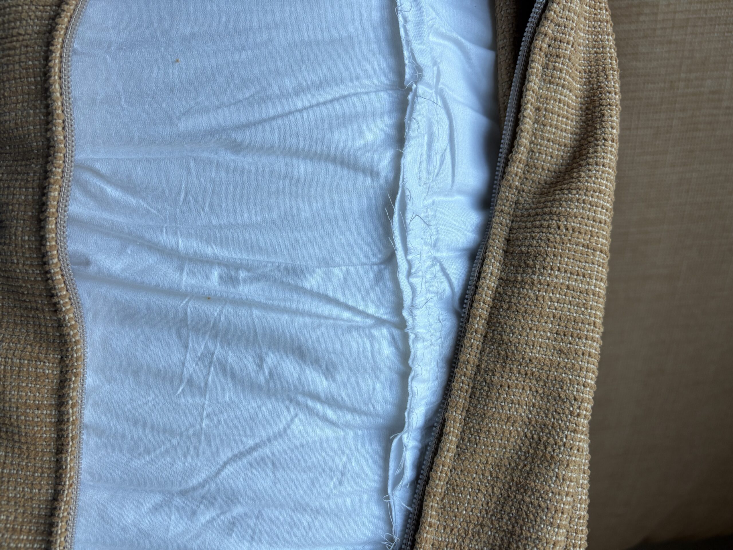 Close-up of a beige fabric cushion cover partially unzipped, revealing the white inner cushion and visible stitching.
