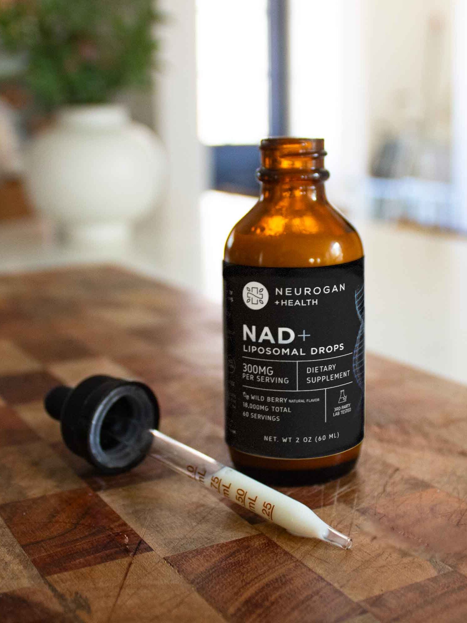 A bottle of Neurogan Health NAD+ Liposomal Drops with a dropper beside it sits on a wooden surface in a well-lit room.
