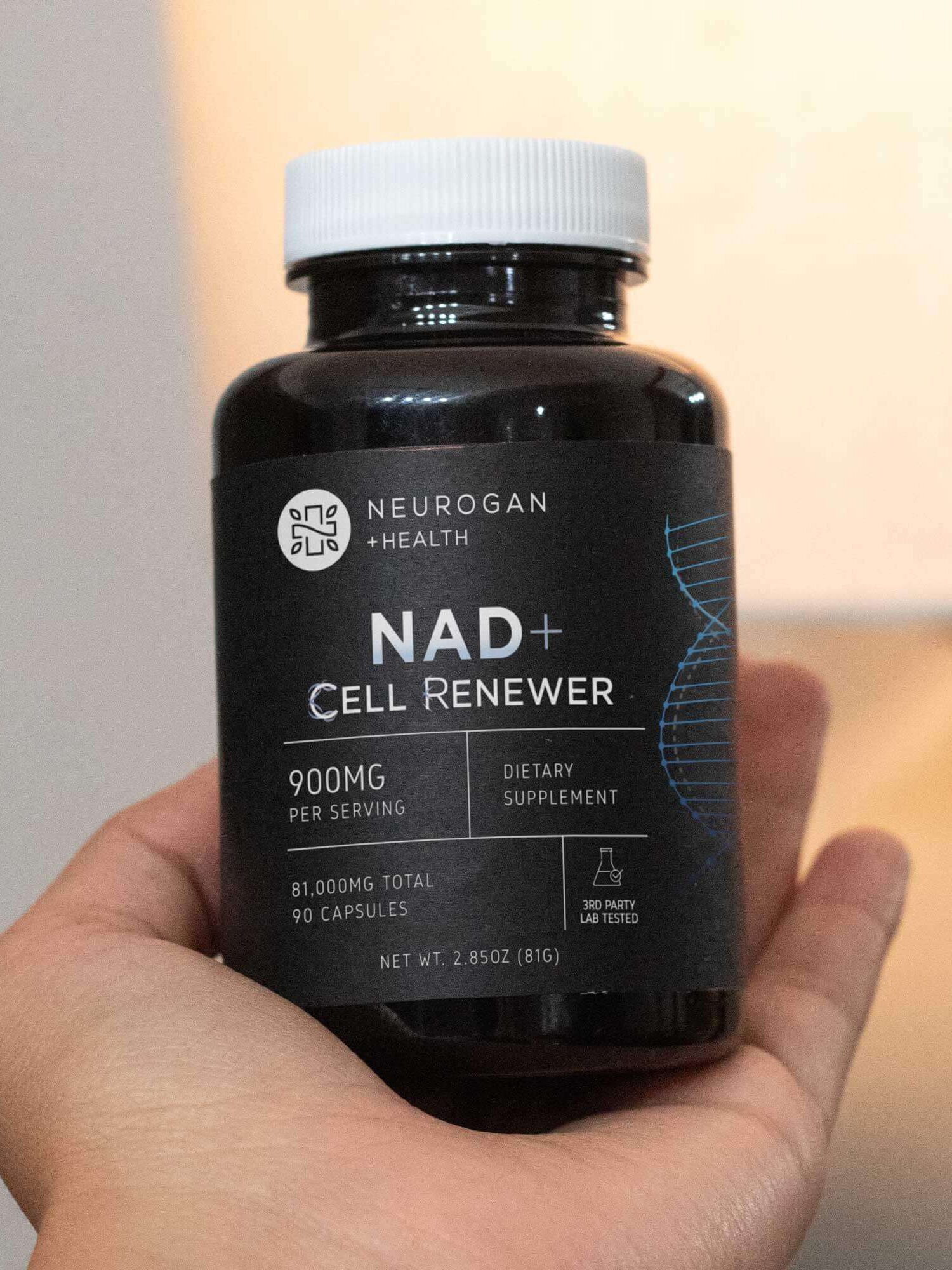 A hand holds a bottle of Neurogan Health NAD+ Cell Renewer dietary supplement, containing 90 capsules with 900mg per serving.