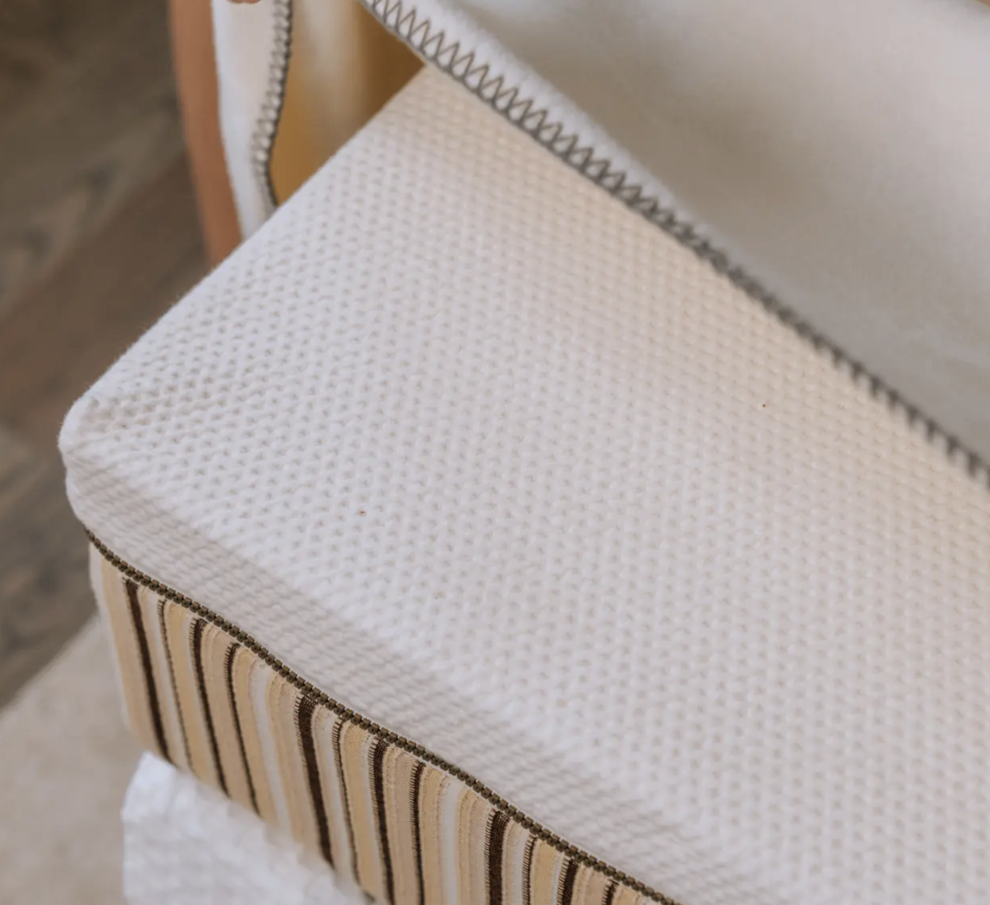 Close-up of a neatly made bed showing a white textured mattress with a striped box spring and a folded blanket at the corner.