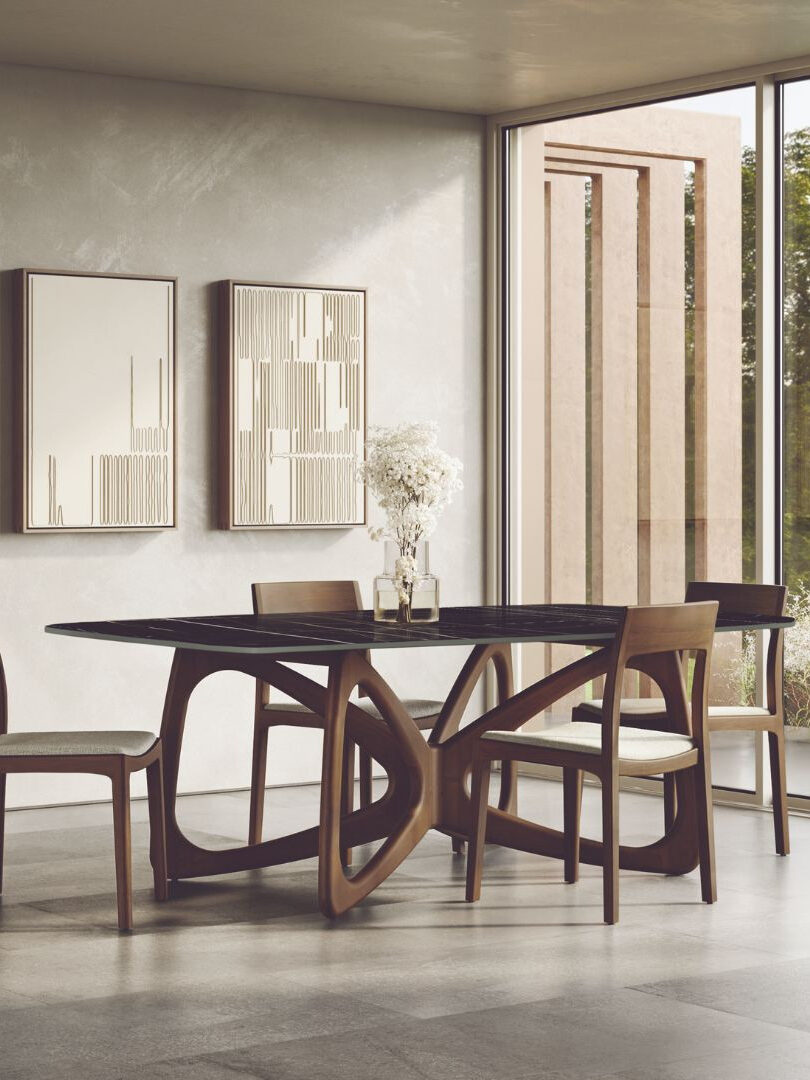 Modern dining room with a black oval table, four wooden chairs, minimalist wall art, large windows, and neutral-toned decor.