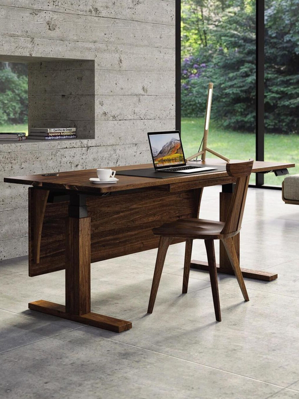 A modern wooden desk with a laptop, monitor, and coffee cup, positioned on a gray tiled floor near a window with a view of greenery outside.