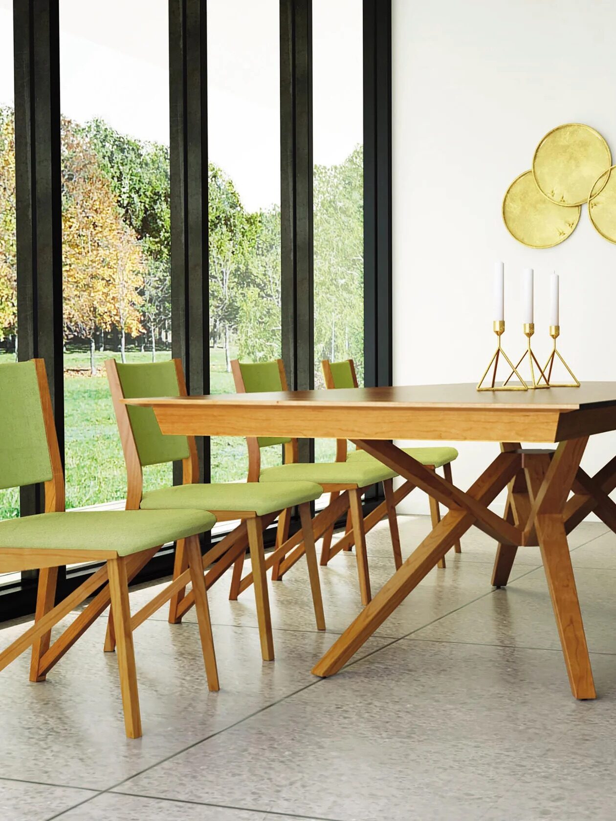 Modern dining room with a wooden table, green cushioned chairs, gold candle holders, and a gold circular wall art, with large windows showing trees outside.