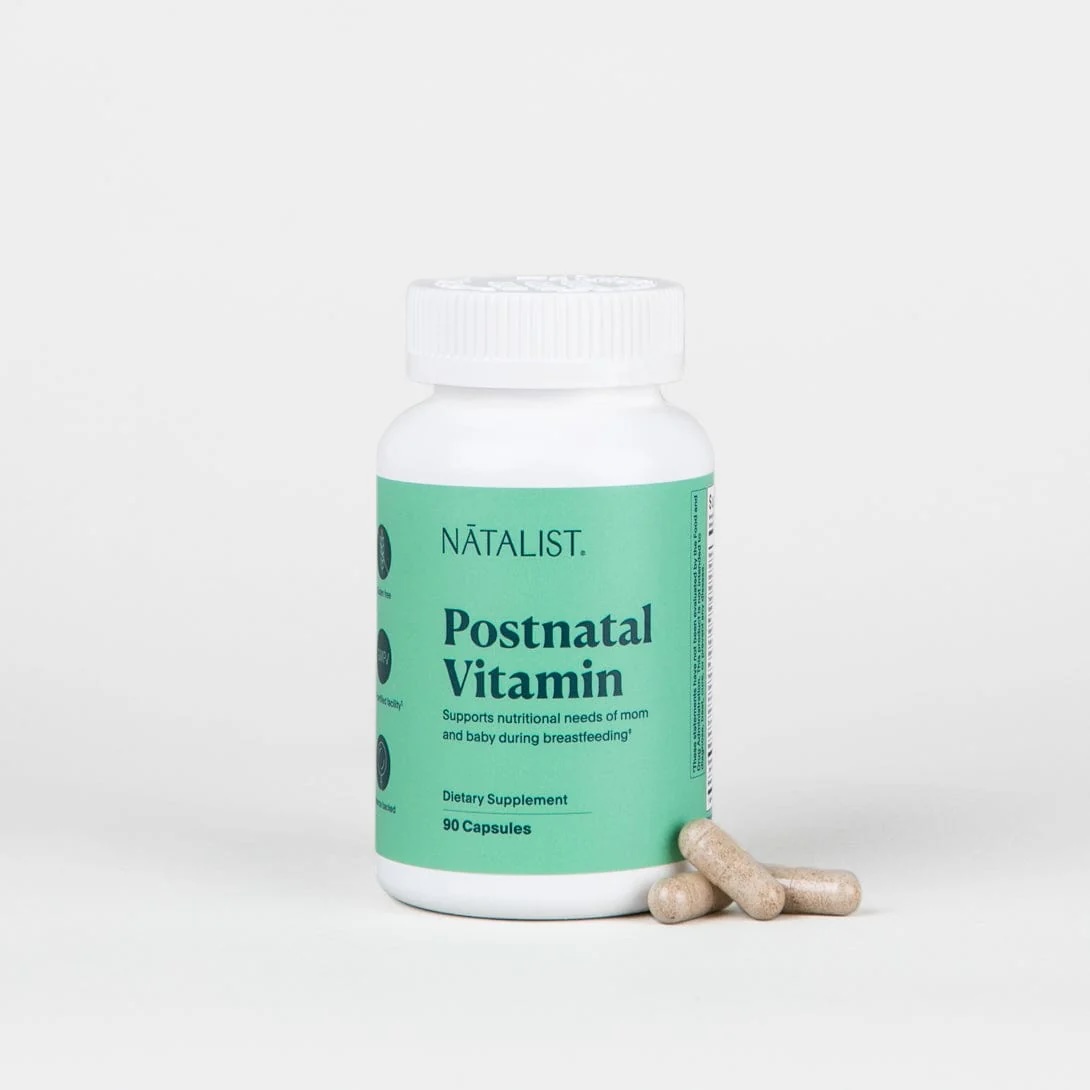 A white bottle labeled "Natalist Postnatal Vitamin" with a green label is shown, along with three beige capsules placed beside it on a plain background.