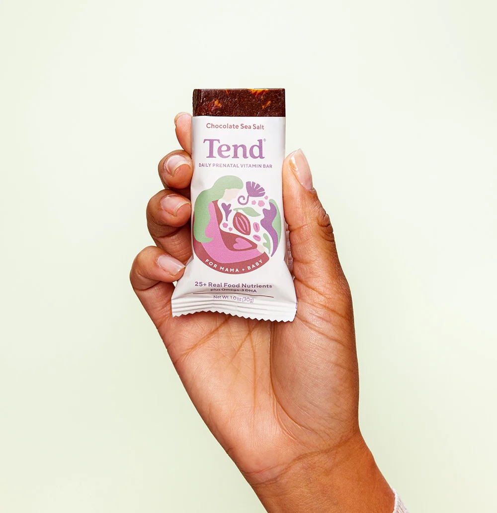 A hand holding a Tend chocolate sea salt daily prenatal vitamin bar against a light background.