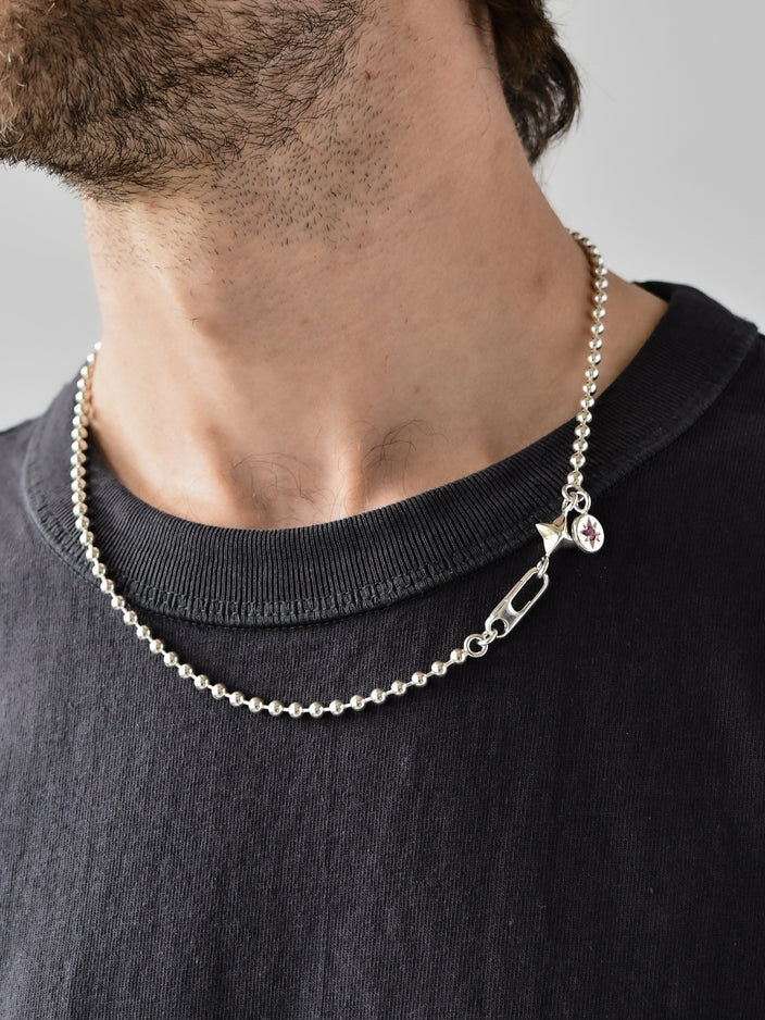 Close-up of a person wearing a silver beaded chain necklace with a decorative clasp and a small pendant, paired with a black crew neck shirt.