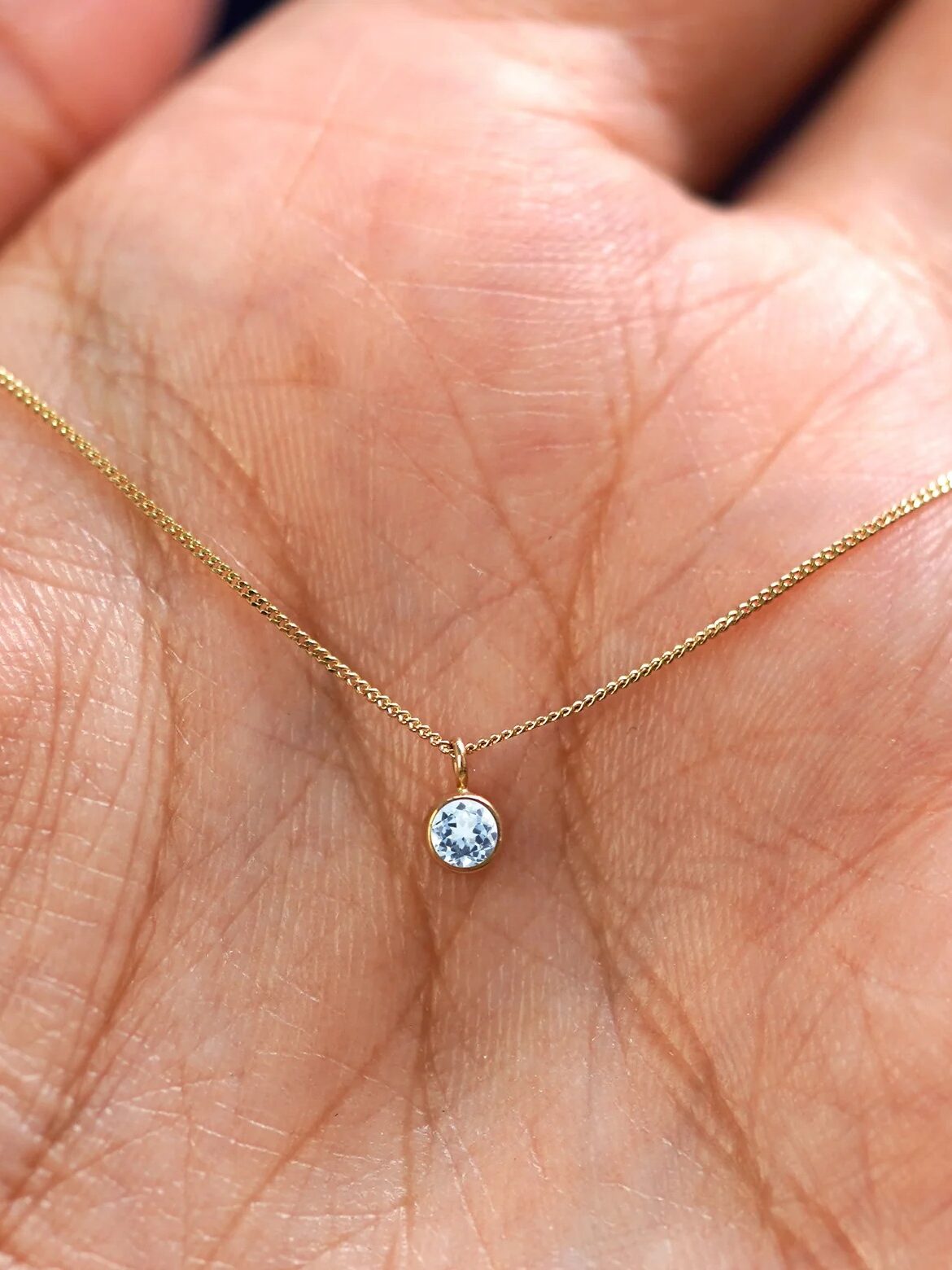 A gold chain necklace with a small round diamond pendant held in the palm of a hand.