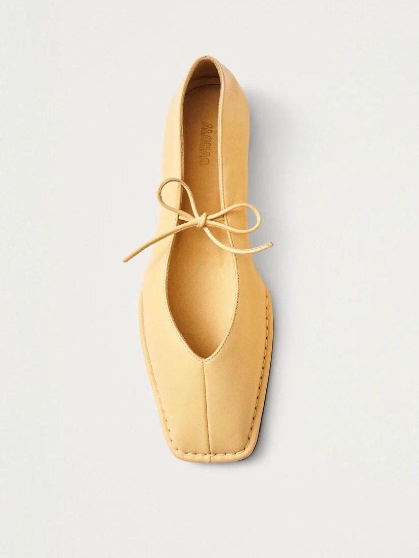 A single tan-colored flat shoe with a square toe and bow-tied laces, photographed from above on a plain white background, channels effortless French girl fashion.