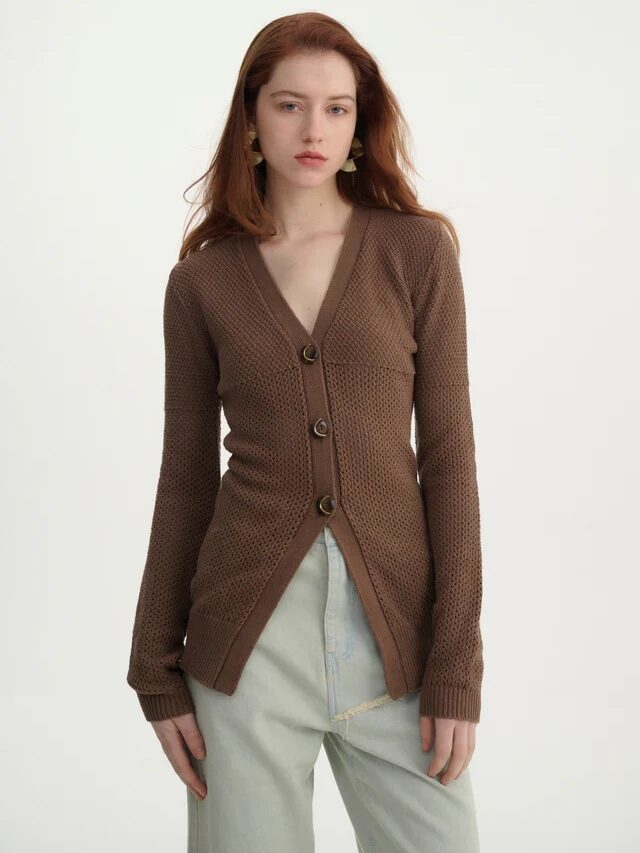 A woman with long red hair wears a brown textured button-up cardigan and light-wash jeans, channeling effortless French girl fashion against a plain white background.