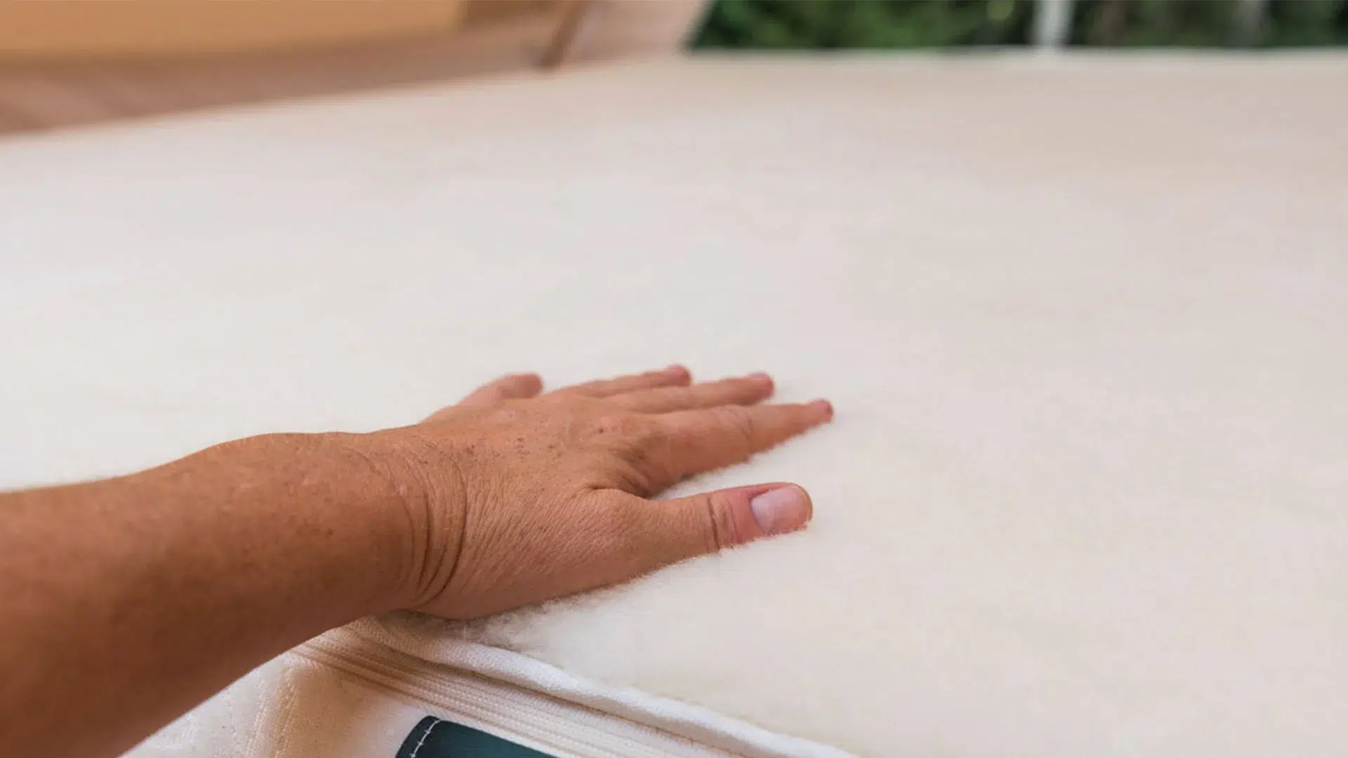 A person's hand pressing down on a soft, white mattress or mattress topper.