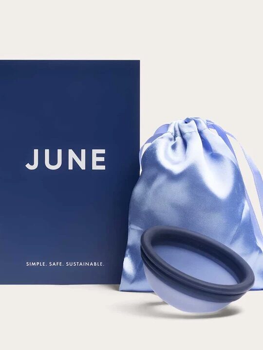 A blue box labeled "JUNE," a silk drawstring pouch, and a collapsible blue menstrual cup are displayed against a neutral background.