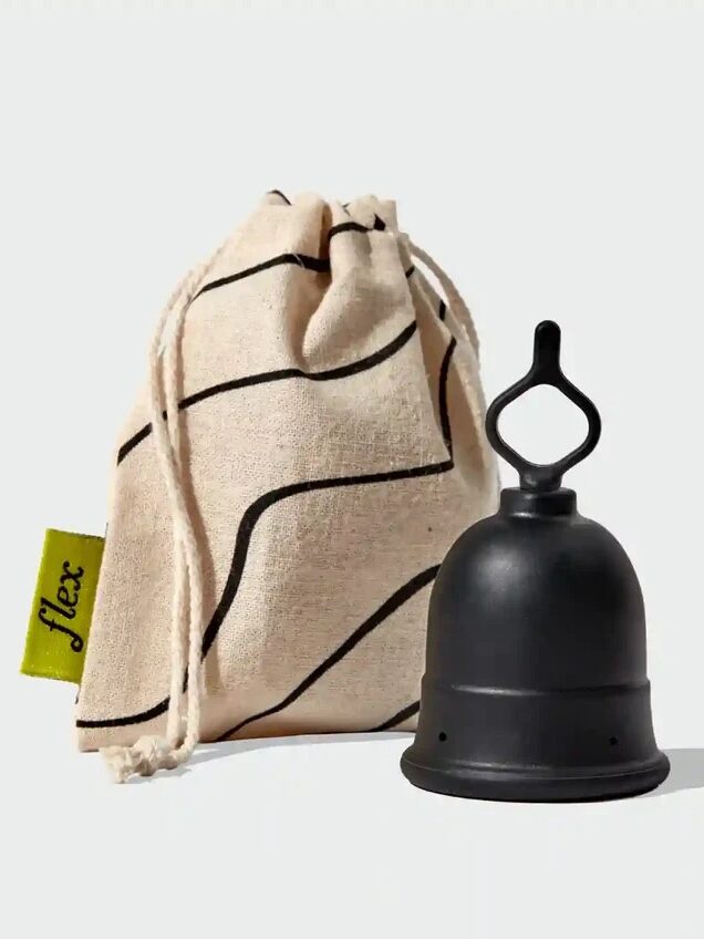 A black menstrual cup with a loop handle is placed next to a beige drawstring storage pouch with a yellow tag labeled "flex.