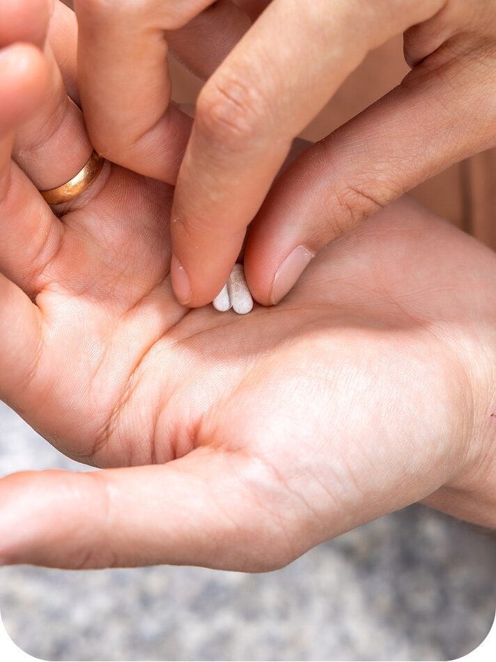 A person holding a white pill between their fingers above the palm of their other hand.