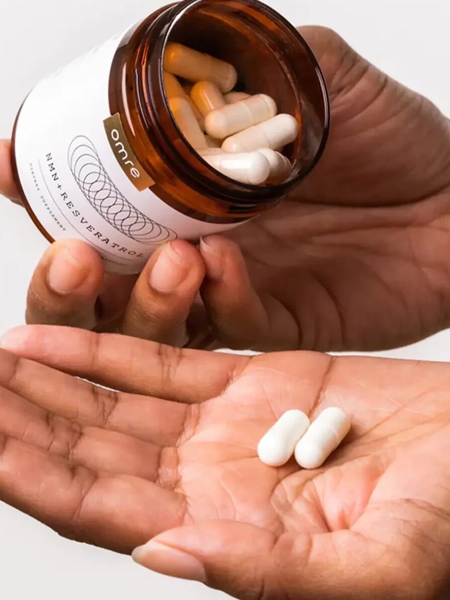 A person pours white capsules from a brown bottle into their hand. Instructions read: take in the morning, with food, 2 capsules a day.