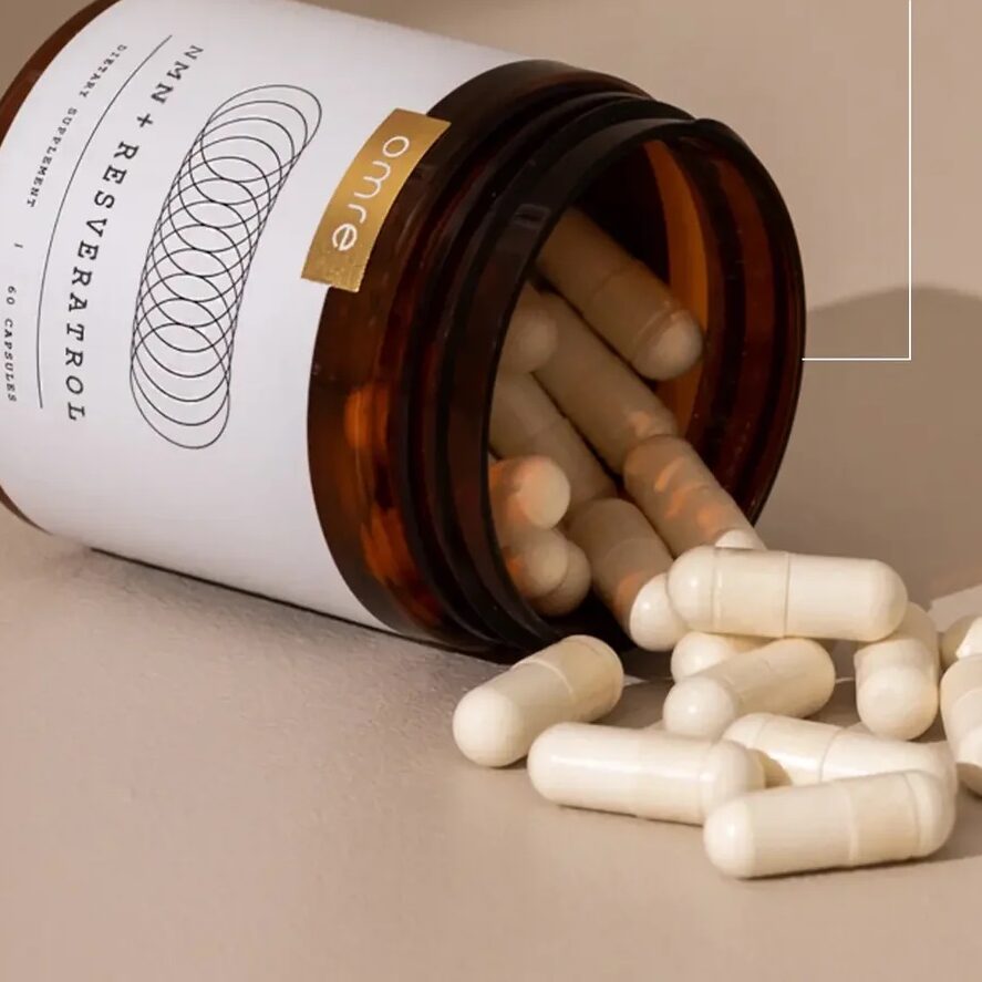 An open brown bottle labeled "Resveratrol" with white capsules spilling out, highlighting 500 mg of 98% pure micronized resveratrol and 500 mg of 99% pure NMN per dose.