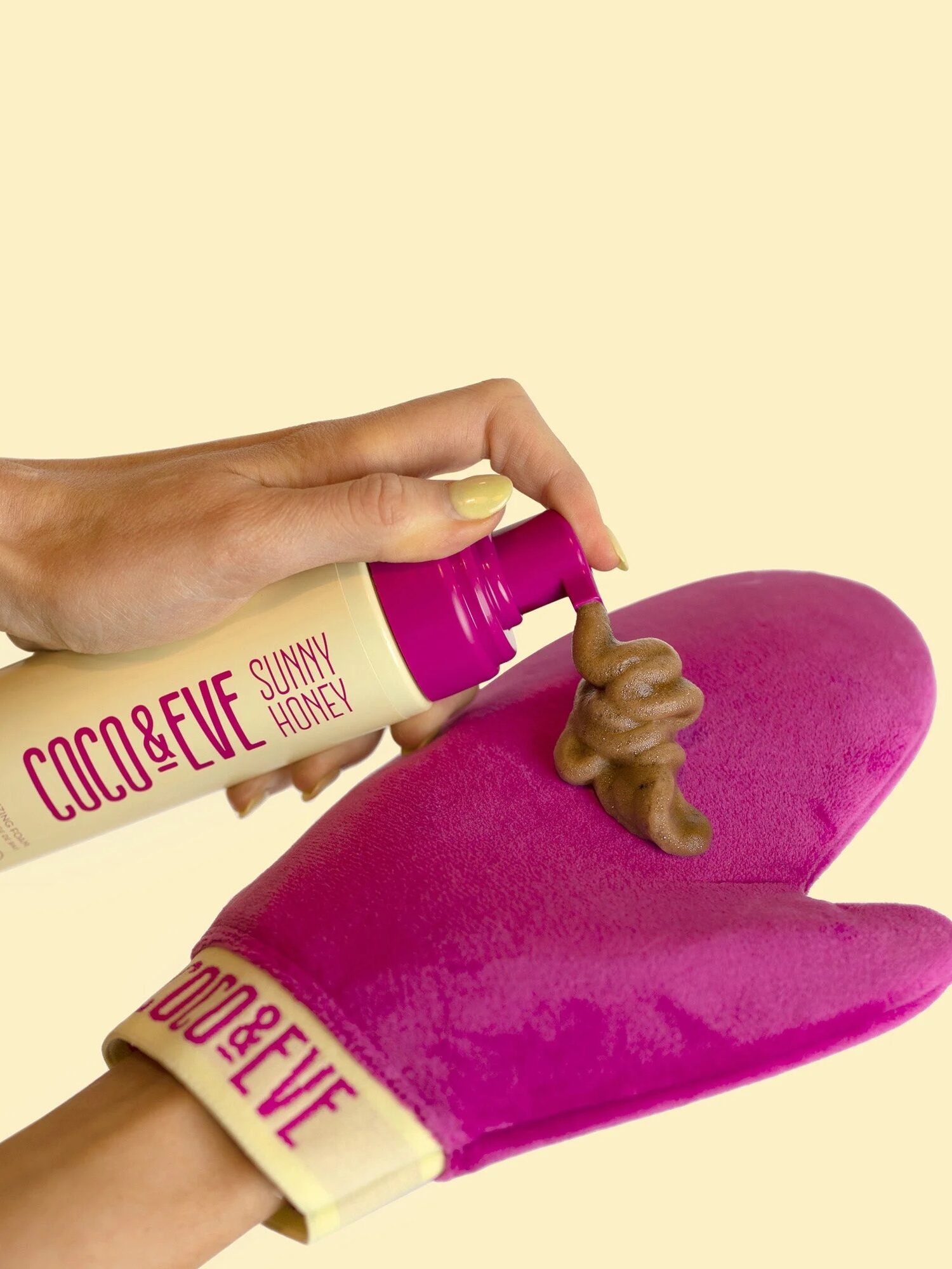 A person dispenses Coco & Eve Sunny Honey tanning foam onto a pink tanning mitt against a light beige background.