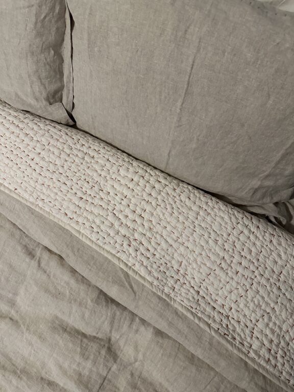 A bed with beige linen sheets and a textured white quilted blanket arranged neatly.