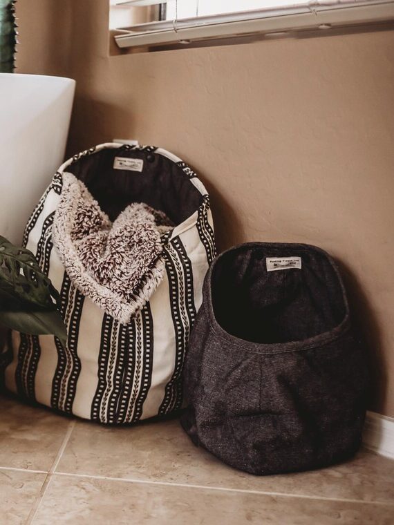 Two potted plants and two fabric pet beds are arranged on a tiled floor near a beige wall and window.