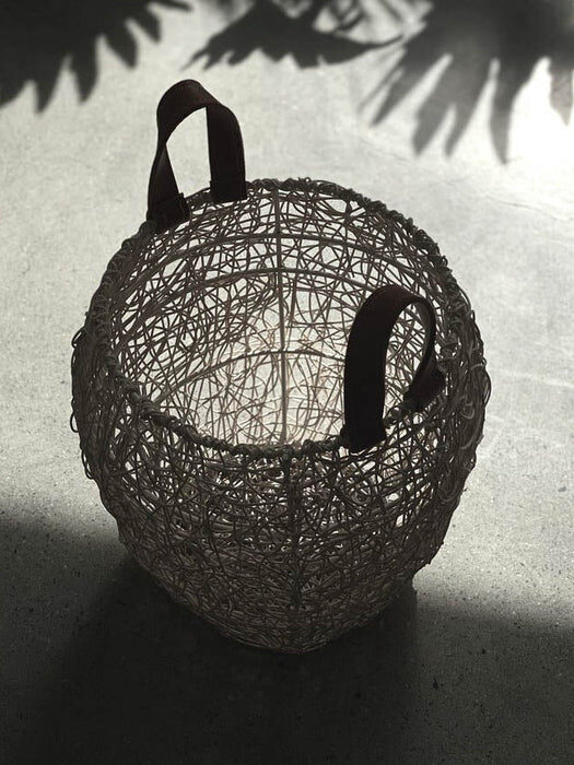 A wire basket with two handles sits on a concrete floor, casting a shadow in bright sunlight.