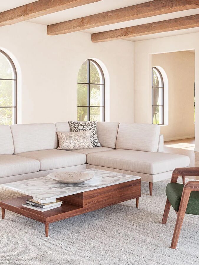 A modern living room with a light sectional sofa, green armchair, wooden coffee table, and exposed ceiling beams, featuring arched windows and neutral decor.