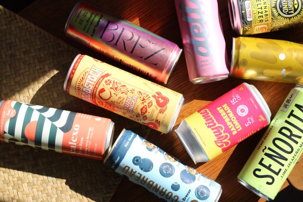 Assorted colorful cans of beverages, including brands like Brez, Senorita, and Squiggly, arranged on a wooden surface in sunlight.