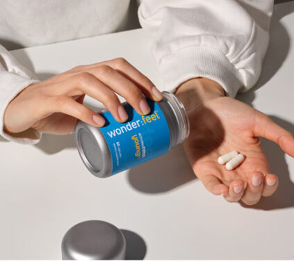 A person pours two white capsules from a blue bottle labeled "wonderfeel" onto their palm while sitting at a white table.