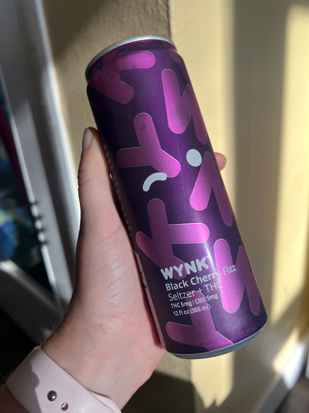 A hand holds a can of WYNK Black Cherry Fizz seltzer with THC and CBD, 12 fl oz, against a sunlit background.