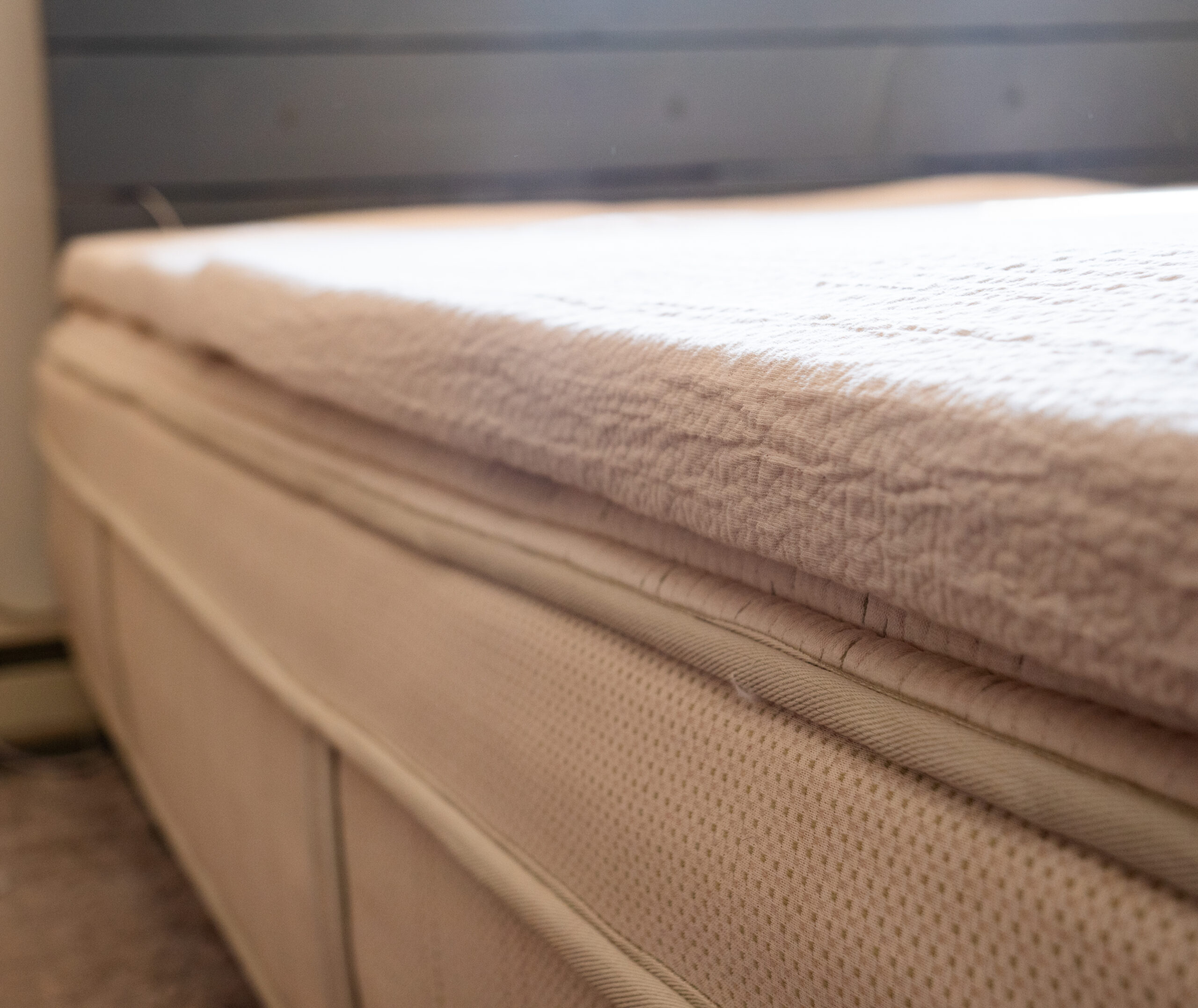 Close-up view of a beige mattress with a textured mattress topper in a softly lit room.